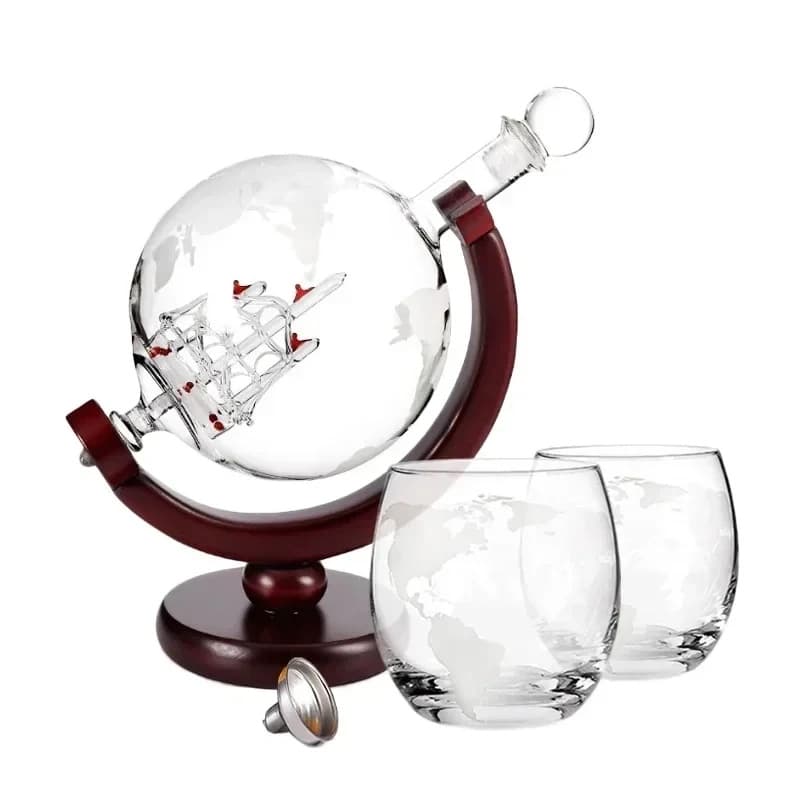 A globe decanter with a glass ship inside on a wooden stand beside two engraved glasses and a funnel