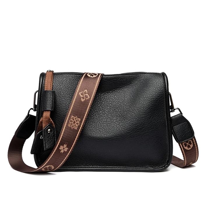 A black leather crossbody bag with a wide brown patterned strap